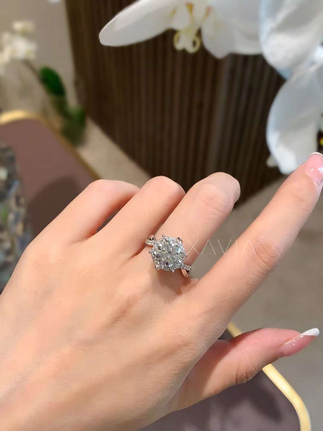 Round halo lab-grown diamond engagement ring with pavé band, shown on model’s hand in natural lighting with white orchid flowers in background